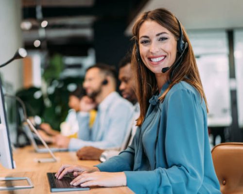 Shot of call center operators working in the office. Female call center agent working with her colleagues in modern office. Smiling beautiful businesswoman working in call center.